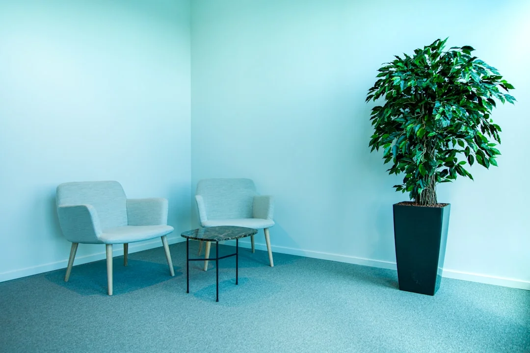 Deux femmes en tenue de travail nettoient un salon moderne à l’aide d’un aspirateur et d’une serpillière.