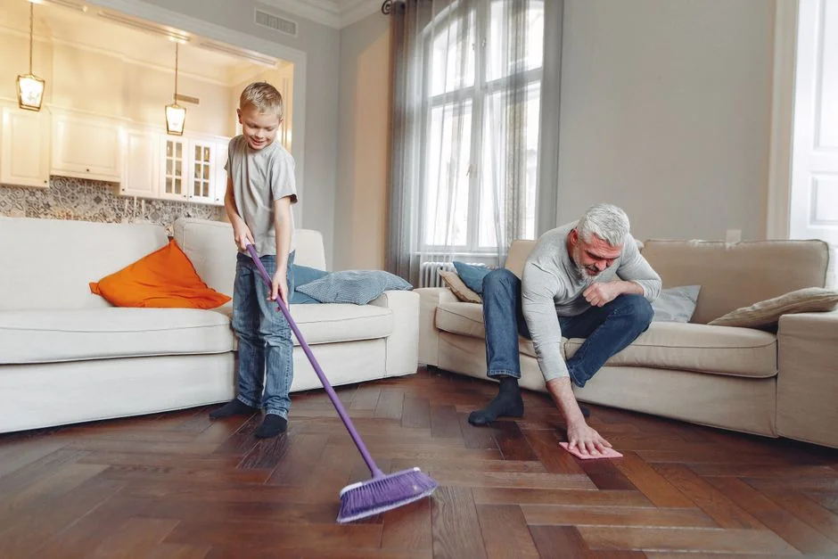 A woman cleaning the floor with a vacuum cleaner while a dog watches attentively. Indoor home setting.